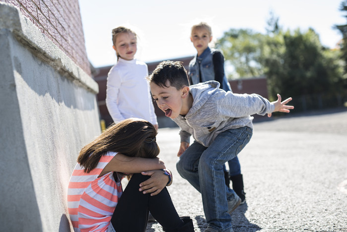 Menino gritando para uma menina com a cabeça baixa em referência ao bullying.