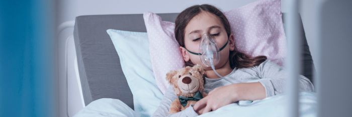 Menina com máscara de oxigênio deitada em leito hospitalar