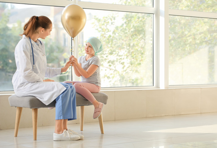 Médica e paciente infantil com câncer segurando, juntas, um balão