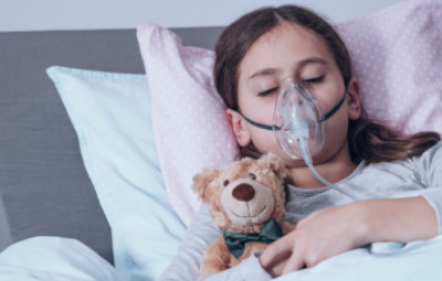 criança doente, usando máscara de oxigênio e abraçada com ursinho