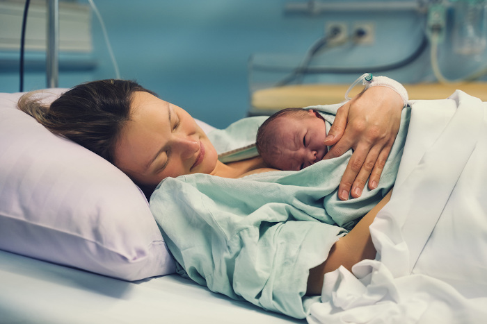 Mulher segurando seu filho recém-nascido deitada em leito de hospital