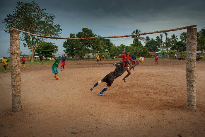 Homens jogando futebol em campo de terra, em Serra Leoa
