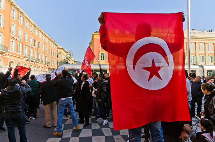 Pessoas em manifestação política na Tunísia; no primeiro plano, um homem segurando a bandeira da Tunísia