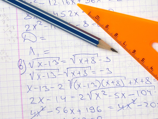 Lápis listrado e régua laranja sobre um caderno com a resolução de uma equação.
