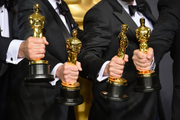 Quatro mãos masculinas segurando, cada uma, uma estatueta do Oscar