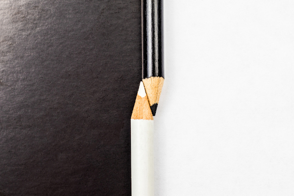 Lápis branco e preto em uma superfície branca e preta ilustrando ideia de contraste e oposição.