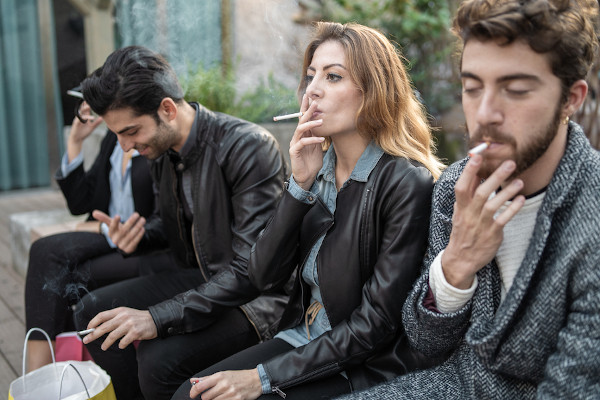 Quatro jovens fumando cigarros ao ar livre.