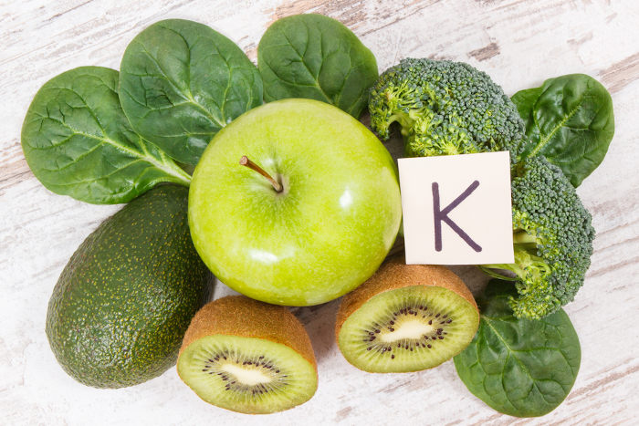 Frutas e vegetais verdes sobre uma mesa de madeira com uma letra K sobre eles.