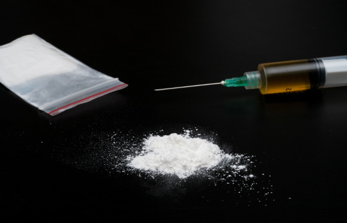 Punhado de cloridrato de cocaína em pó, ziplock com cocaína em pó e seringa com cocaína líquida, em fundo escuro