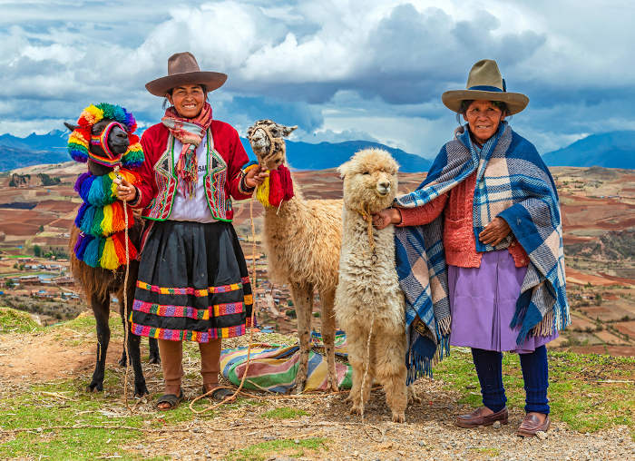 Duas mulheres indígenas bolivianas segurando, ao todo, três lhamas, em região montanhosa