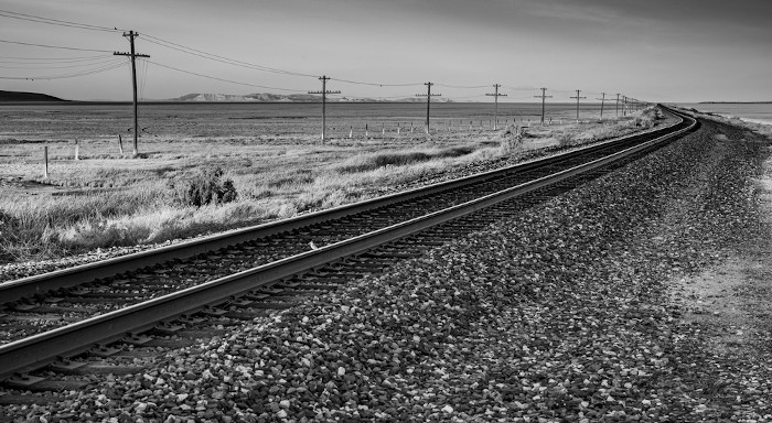  Imagem em preto e branco de postes próximos a uma ferrovia.