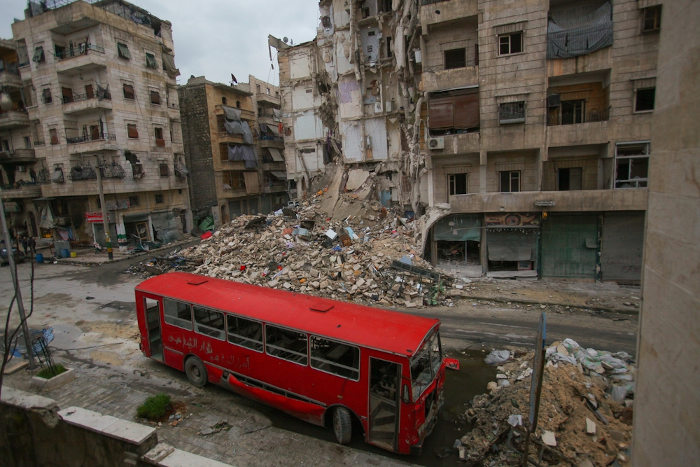 Ônibus vermelho em frente a um prédio destruído em Aleppo, na Síria.