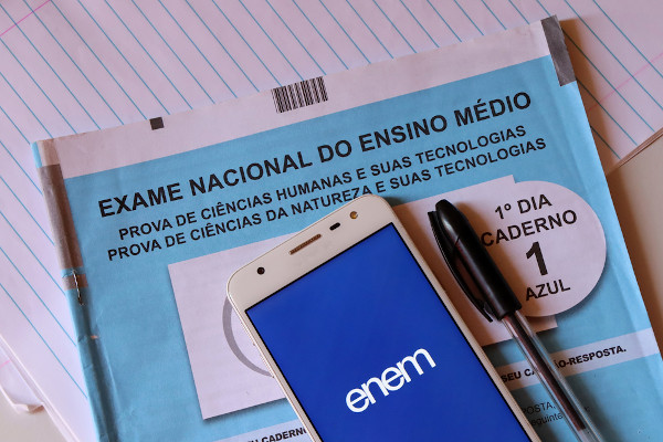 Celular aberto no aplicativo do Enem, ao lado de uma caneta preta e sobre um caderno de prova do exame.