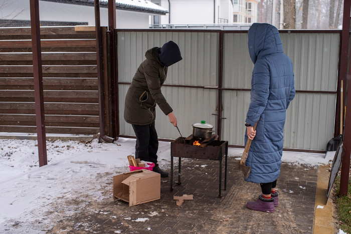 Duas pessoas cozinhando um pouco de comida em um fogão improvisado, na região de Kiev, na Ucrânia, em março de 2022.