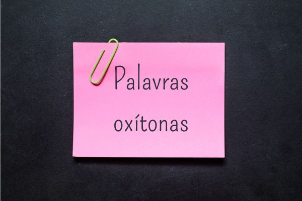 Post-it, com um clipe de papel e o escrito “palavras oxítonas”, colado em um quadro-negro.