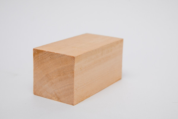 Bloco de madeira, no formato de um paralelepípedo, sobre uma superfície branca.