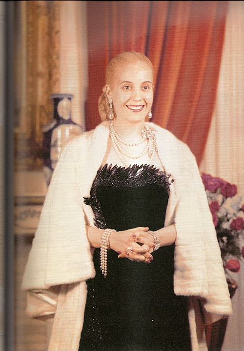Eva Perón trajando roupas de festa e sorrindo de mãos dadas.