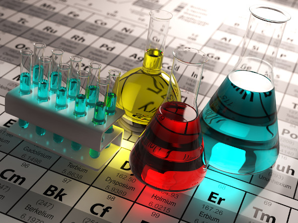 Tubos e frascos de laboratório, com substâncias químicas coloridas, sobre uma Tabela Periódica.