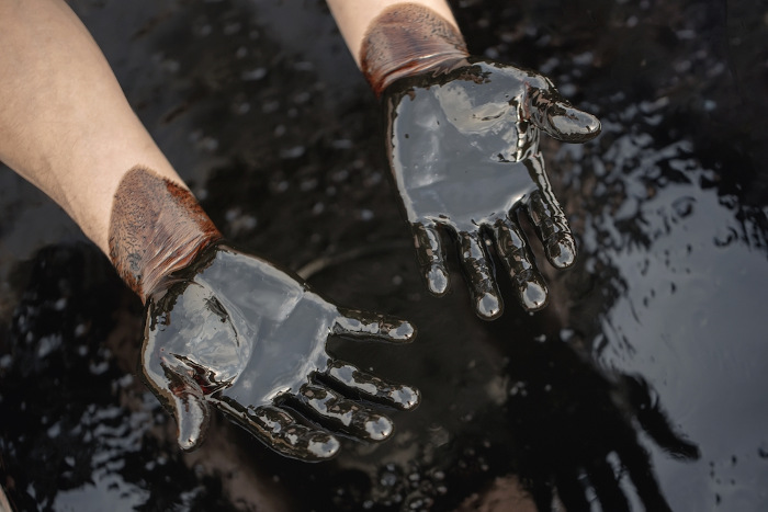  Vista aproximada das mãos de uma pessoa sujas de petróleo em sua forma pura.