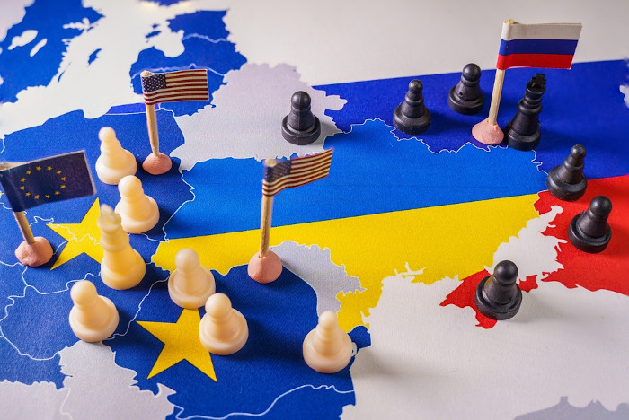 Bandeira dos Estados Unidos, Rússia e União Europeia ao lado de peças de xadrez, ao redor do mapa da Ucrânia.