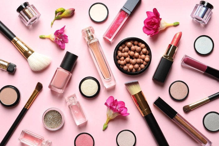 Diversos produtos de beleza sobre uma superfície rosa.