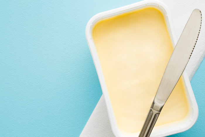 Vista superior de uma faca sobre um pote aberto de margarina.