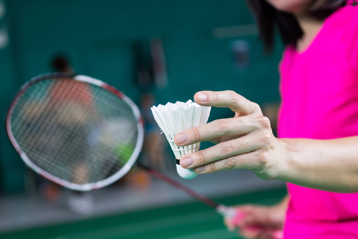 Atleta segurando uma peteca branca com uma mão e a raquete com a outra, os equipamentos do badminton. 