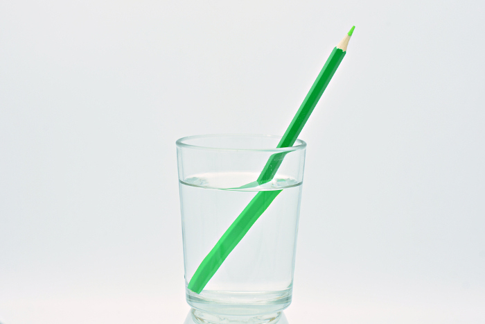 Green pencil inside a glass of water illustrating the concept of light refraction.  In the image, the pencil appears broken.