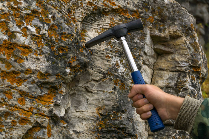 Geólogo, o profissional da área da geologia, colhendo uma amostra de rocha com um martelo geológico.