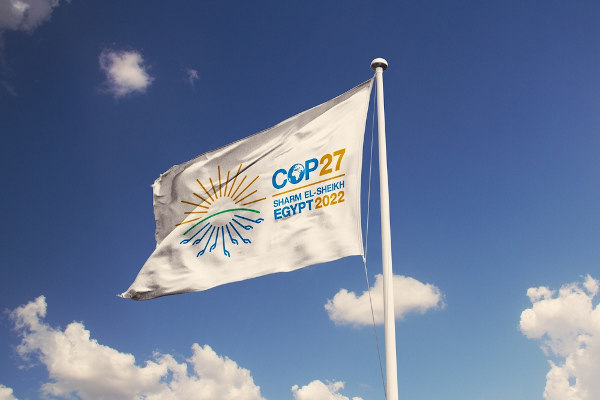 Bandeira hasteada com logo da COP27, céu azul ao fundo.
