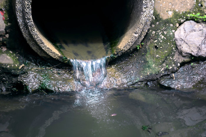 Esgoto sendo derramado em corpo hídrico, um exemplo de poluição da água.