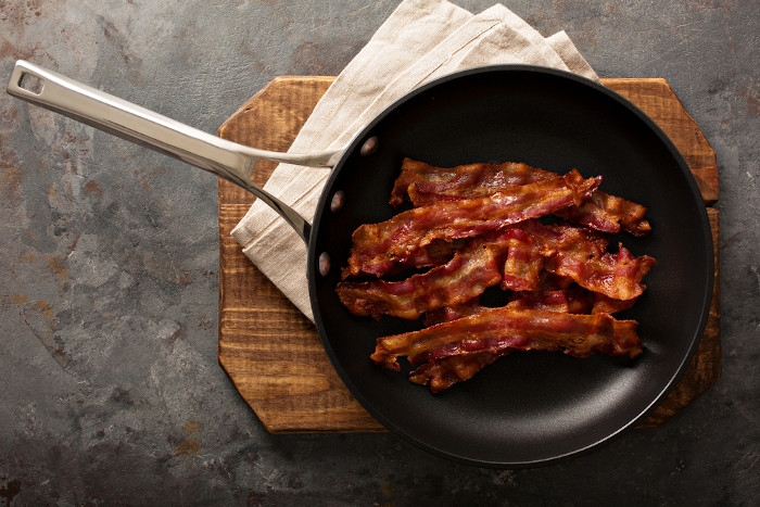 Vista superior de tiras de bacon em uma frigideira representando a ideia de consumo de nitratos derivados de embutidos.