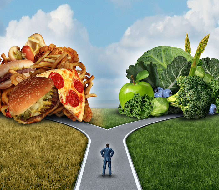 Homem no meio de uma estrada onde há, de um lado, hambúrgueres e pizzas, alimentos ultraprocessados, e, do outro, vegetais.