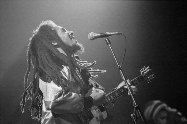 Bob Marley cantando em um microfone e tocando guitarra durante uma apresentação.