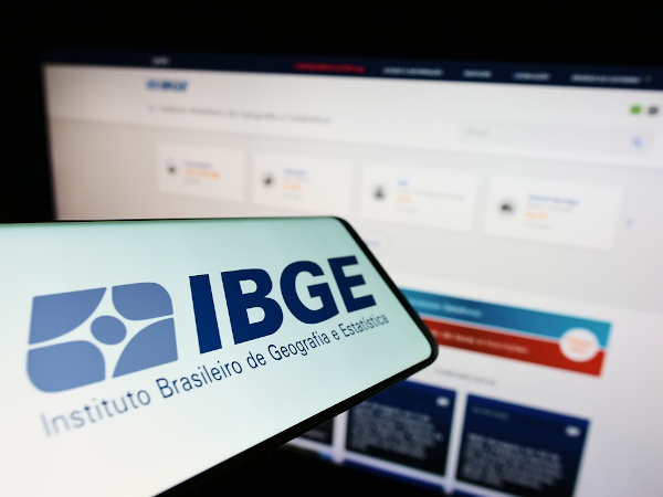 Celular com logo do IBGE em frente a tela de computador.