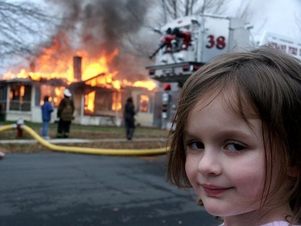Menina branca em primeiro plano e, ao fundo, uma casa pegando fogo