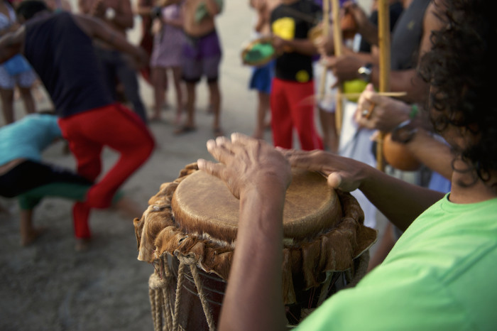 Pessoas tocando tambor e berimbau em uma roda de capoeira.