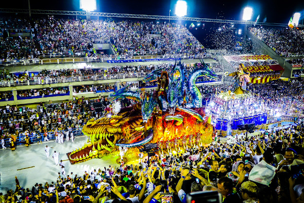 Carro alegórico com formato de um dragão, sendo assistido por uma multidão em um desfile, durante o Carnaval no Brasil.