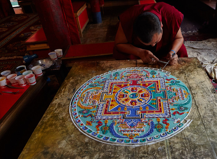 Monge tibetano construindo uma mandala com areia colorida como representação do uso da mandala na religião.