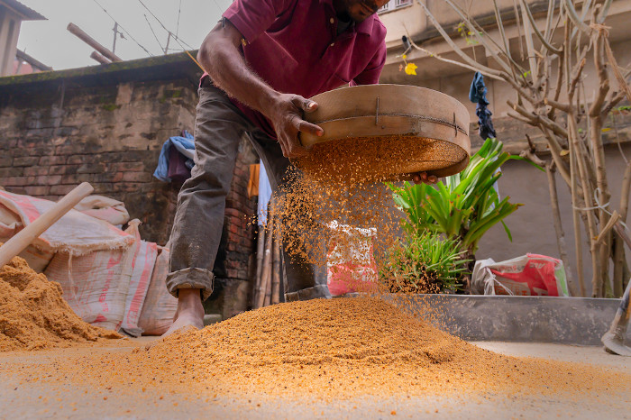 Homem fazendo peneiração para separar grãos de areia de diferentes tamanhos, um processo que se difere da levigação.