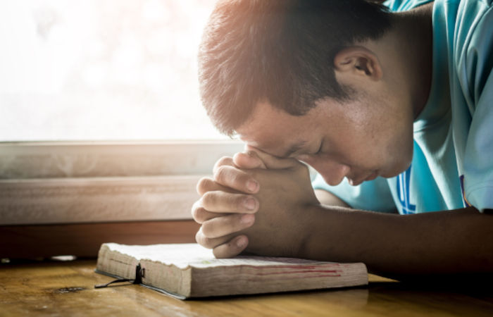 Homem ajoelhado orando com as mãos apoiadas em uma Bíblia, prática intensificada na Quaresma.