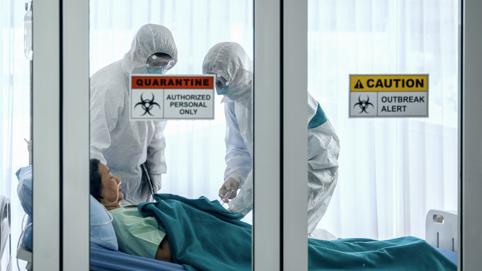 Pessoa hospitalizada em decorrência da covid-19 recebendo atendimento de dois profissionais da saúde com roupas de proteção.