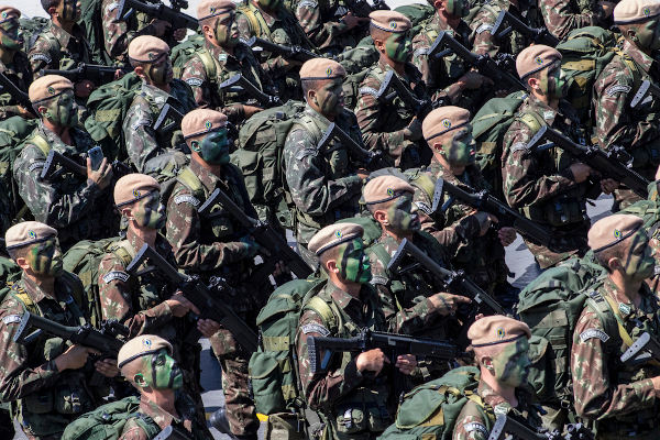 Soldados do Exército Brasileiro com trajes, pintura facial e armas em punho.