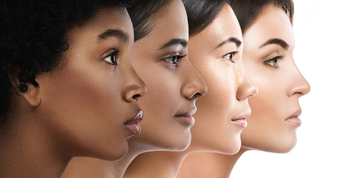Vista lateral do rosto de quatro mulheres com diferentes cores de pele, a qual faz parte do sistema tegumentar.