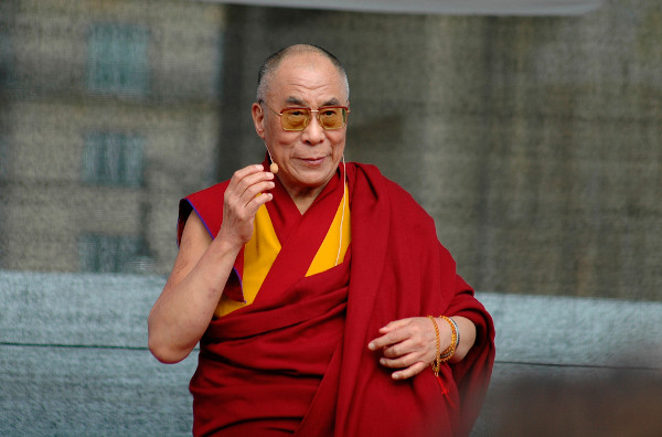 Atual Dalai Lama vestido com uma roupa vermelha e amarela, usando óculos.