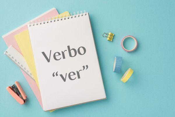 Caderno com o escrito “verbo ‘ver’” próximo a outros materiais de estudo.