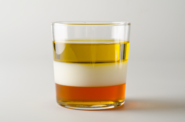 Copo de vidro contendo os fluidos mel, leite e óleo.