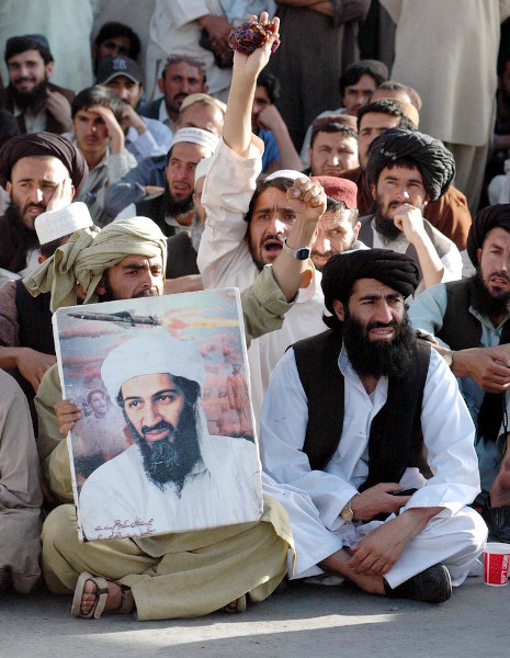 Homens com roupas típicas do Paquistão sentados no chão, segurando um cartaz com a foto de Osama bin Laden.
