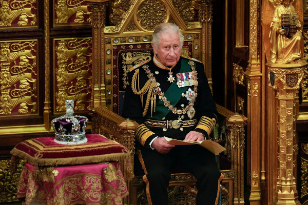 Rei Charles III sentado em trono ao lado de coroa.
