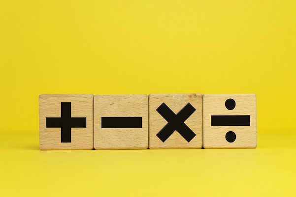 Blocos de madeira com os símbolos das quatro operações matemáticas básicas: adição, subtração, multiplicação e divisão.